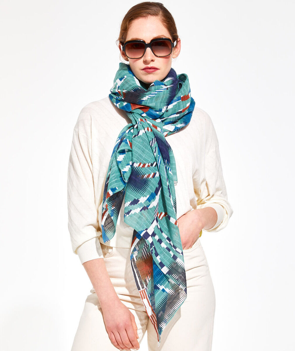 Frau mit Sonnenbrille trägt ein bunt gemustertes Baumwolltuch mit den Hauptfarben Grün, Blau und Orange. Das Tuch ist um den Hals geschlungen, modisch und für den Frühling oder Sommer geeignet.