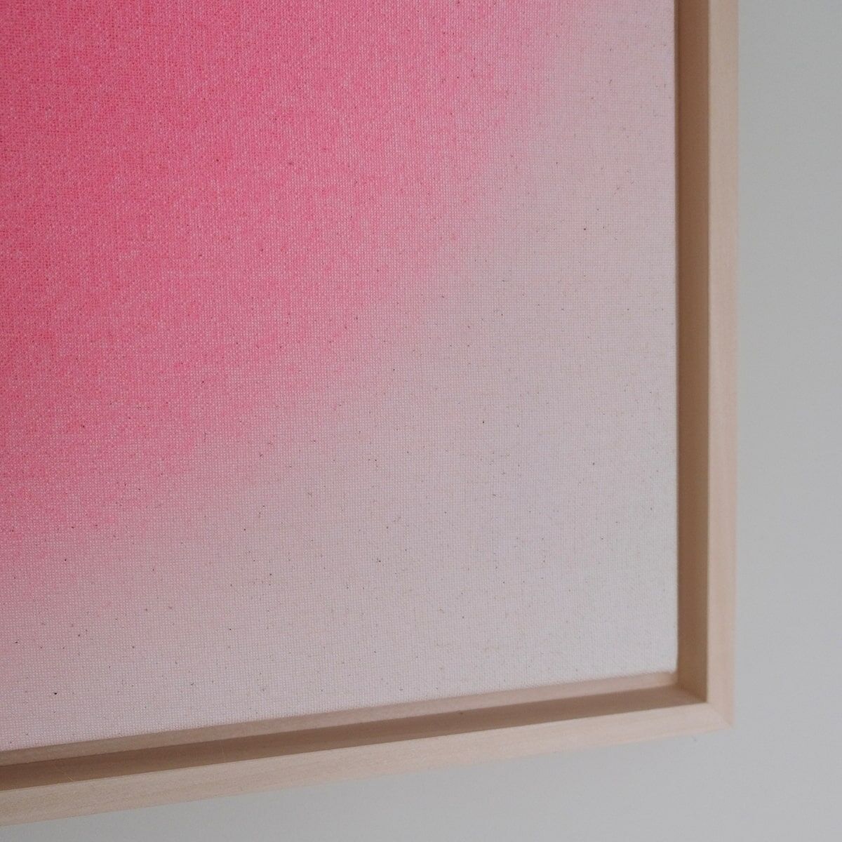 Abstrakte Kunst: Ein quadratisches Bild (59x59cm) mit einem sanften Farbverlauf von kräftigem Pink oben links zu Weiß unten rechts. Das Kunstwerk ist in einem schlichten, naturfarbenen Holzrahmen gefasst.