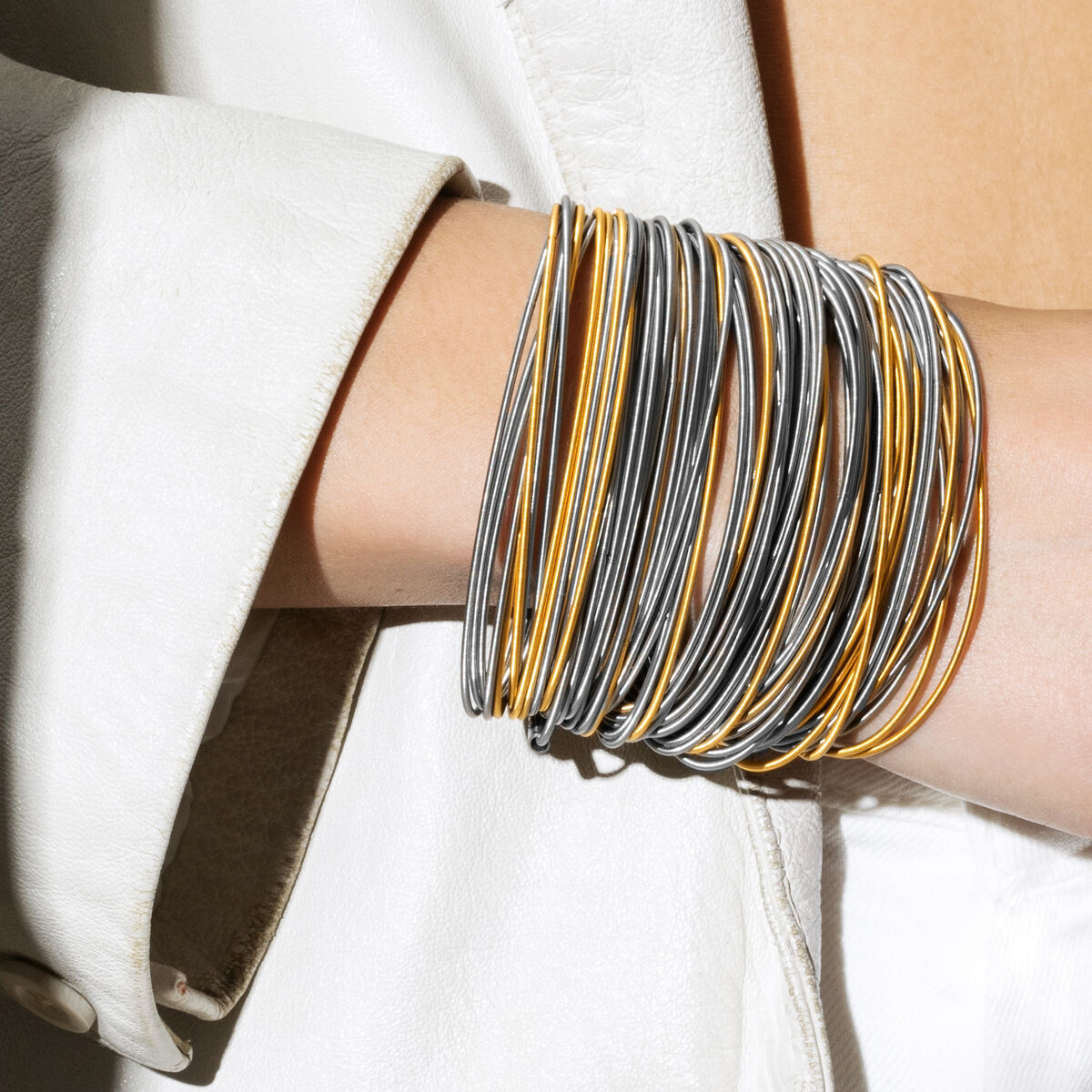 Mehrreihiges Armband in Silber- und Goldoptik am Handgelenk einer Person, stilvoll kombiniert zu einem weißen Jacket, modernes und elegantes Schmuckstück für Damen.