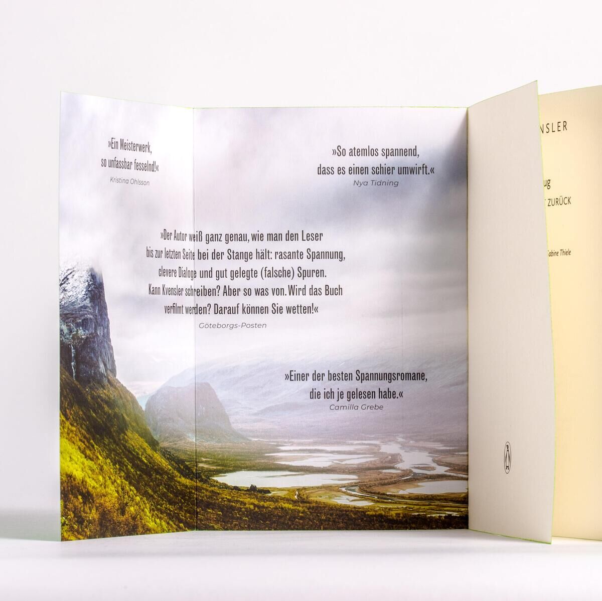 Das Bild zeigt das Buch 'Kvensler, U: Ausflug - Nur einer kehrt zurück'. Im Vordergrund sieht man ein aufgeschlagenes Buch mit einem Landschaftsbild von Bergen und einer weiten Landschaft sowie einem Zitat auf der linken Buchseite. Die rechte Buchseite und der danebenliegende, zugeklappte Buchdeckel sind in hellen Farben dargestellt, wobei der Buchrücken grün ist. Das Bild hebt die visuelle Gestaltung und die Naturthematik hervor.