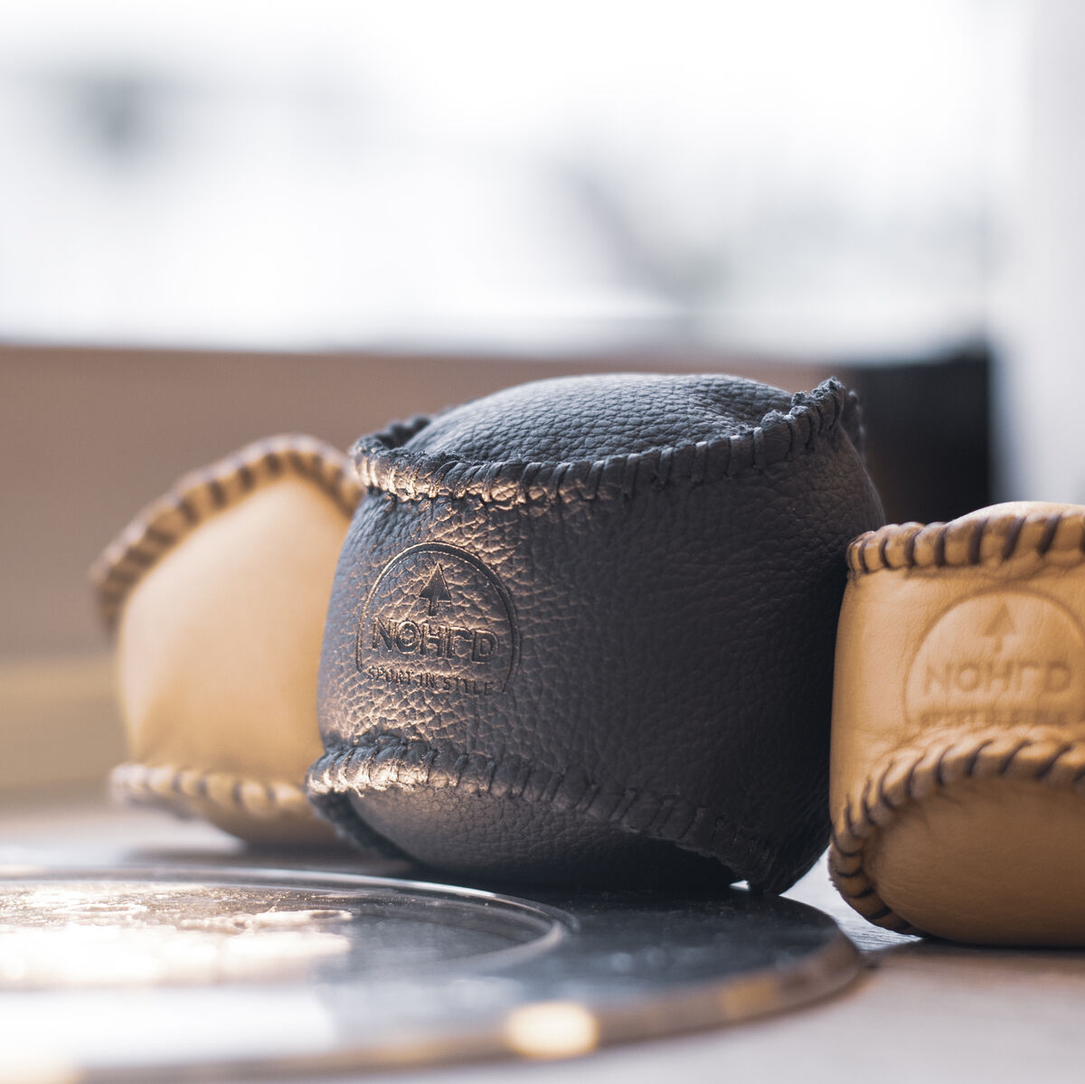 Drei HaptikBälle aus Leder in Schwarz und Beige auf einer Tischoberfläche. Sie haben eine strukturierte Oberfläche und sind handgroß, geeignet für Ergotherapie und Stressabbau.