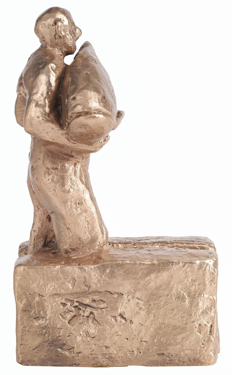 Eine bronzene Skulptur von Christoph Fischer mit dem Titel 'Hoffnungsträger'. Die Figur stellt eine Person dar, die ein großes Bündel oder Paket in den Armen hält und auf einem rechteckigen Sockel steht.