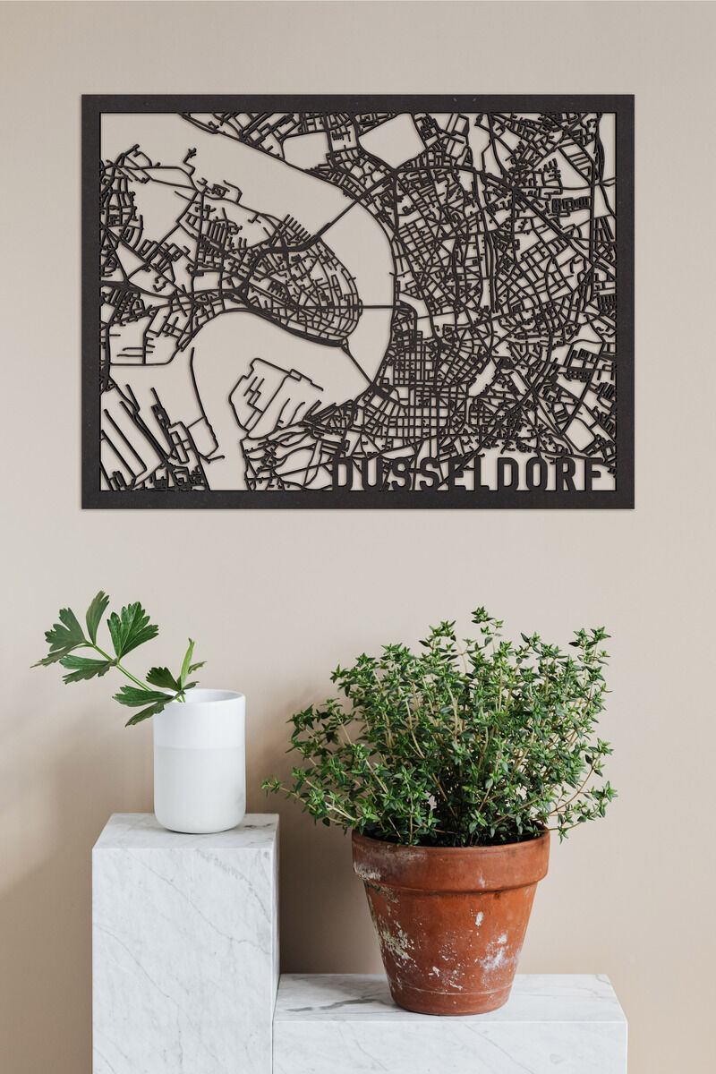 Ein kunstvolles, schwarzes Holzschnitt-Relief einer Stadtkarte von Düsseldorf ist an einer beigen Wand befestigt. Darunter steht ein weißer Zylinderbehälter auf einer weißen Sockelstruktur aus Marmor und ein getöpferter Pflanzentopf mit grünen Kräutern daneben.