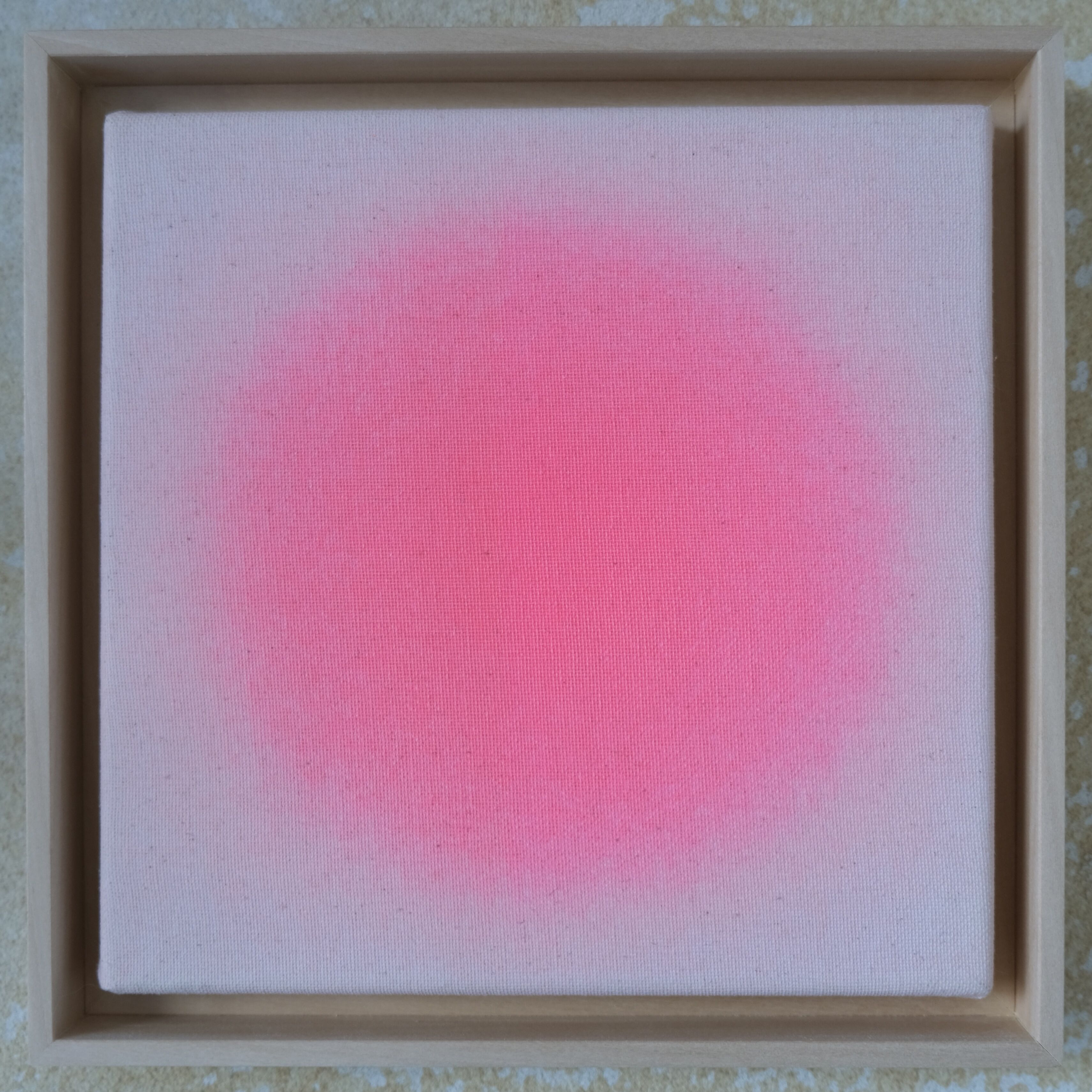 Quadratisches Kunstwerk »Sorbet« mit zartem, strahlendem Pinkverlauf auf ungebleichter Leinwand in Naturbeige. Rund um das Pink wirkt die Farbe zum Rand hin weicher. Das Bild ist in einem schlichten, hellen Lindenholzrahmen gefasst und auf einer Natursteinwand platziert.
