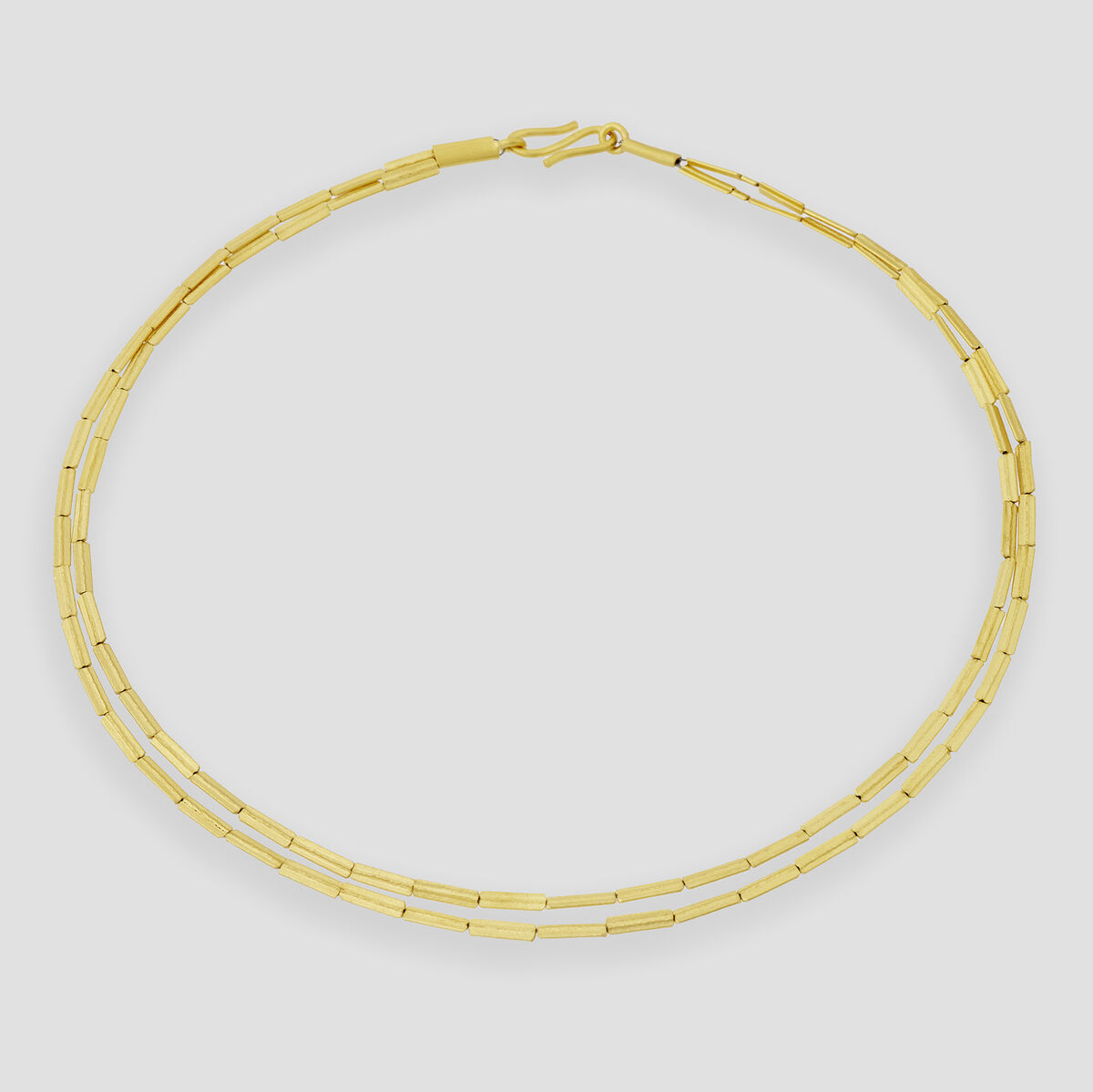 Fotografie eines eleganten, zweireihigen Colliers in Halmketten-Optik, aus silbernem Metall gefertigt und mit feinem Gold überzogen. Das Schmuckstück liegt auf hellem, neutralem Untergrund und wirkt modern sowie hochwertig verarbeitet.