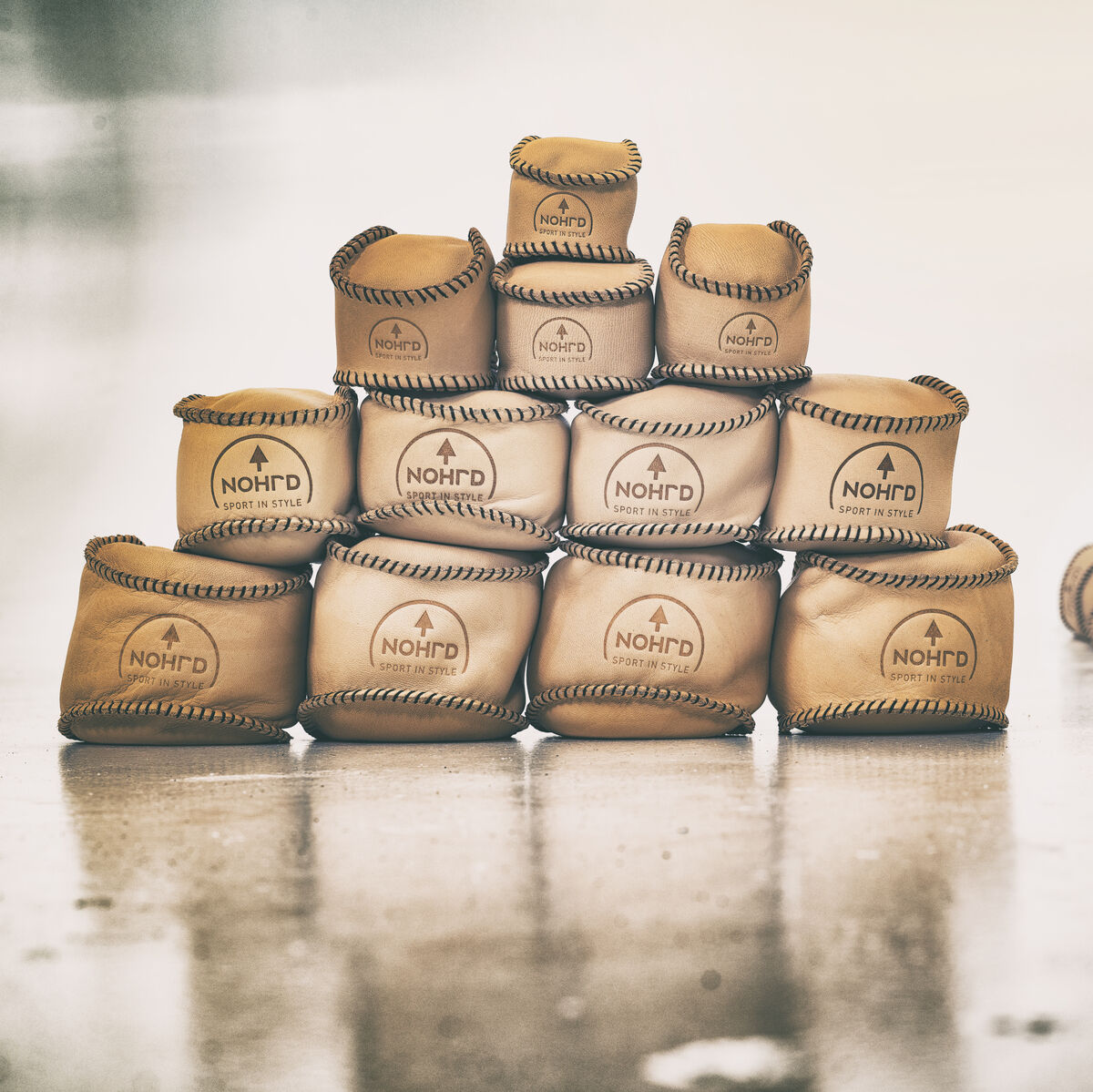 Eine Pyramide aus NOHrD HaptikBällen aus Naturmaterialien steht auf einem glänzenden Boden. Einige lose Bälle liegen im Hintergrund. Die HaptikBälle sind in beige und braun gehalten und erinnern an handgefertigte Produkte.