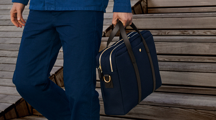 Person in dunkelblauer Kleidung trägt eine dunkelblaue Business-Tasche mit schwarzen Griffen und goldfarbenen Reißverschlüssen