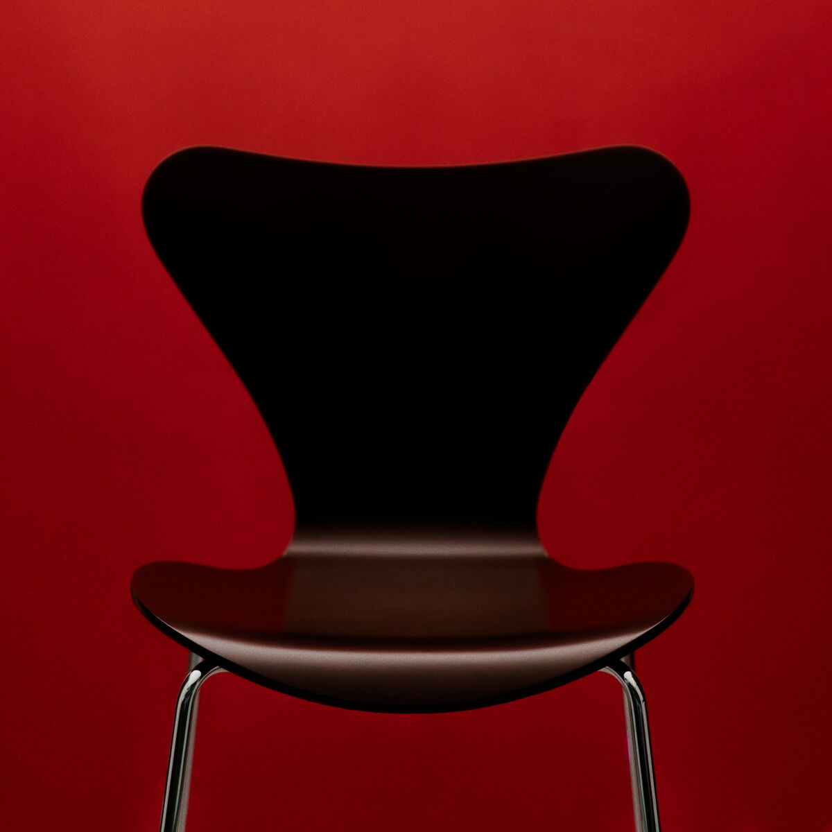 Designstuhl "Serie 7" Edition Verner Panton von Fritz Hansen, Variante Brown mit lackierter Buchenfurnierschale und Stahlrohrgestell, frontal vor leuchtend rotem Hintergrund, Sitzhöhe 46 cm, elegantes und modernes Design, klar konturierte Form.