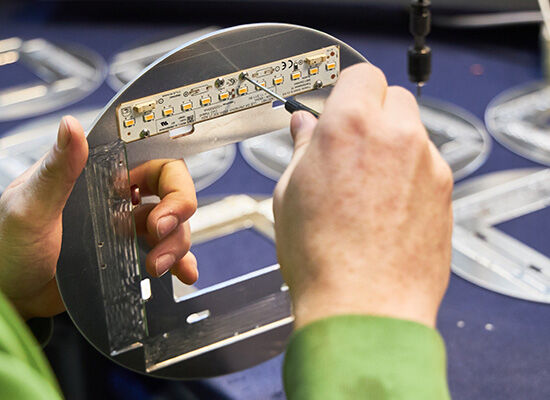 Eine Person hält eine Leuchttafel in der Hand und setzt mit einem Schraubenzieher LED-Leuchten auf einen runden Metallrahmen.