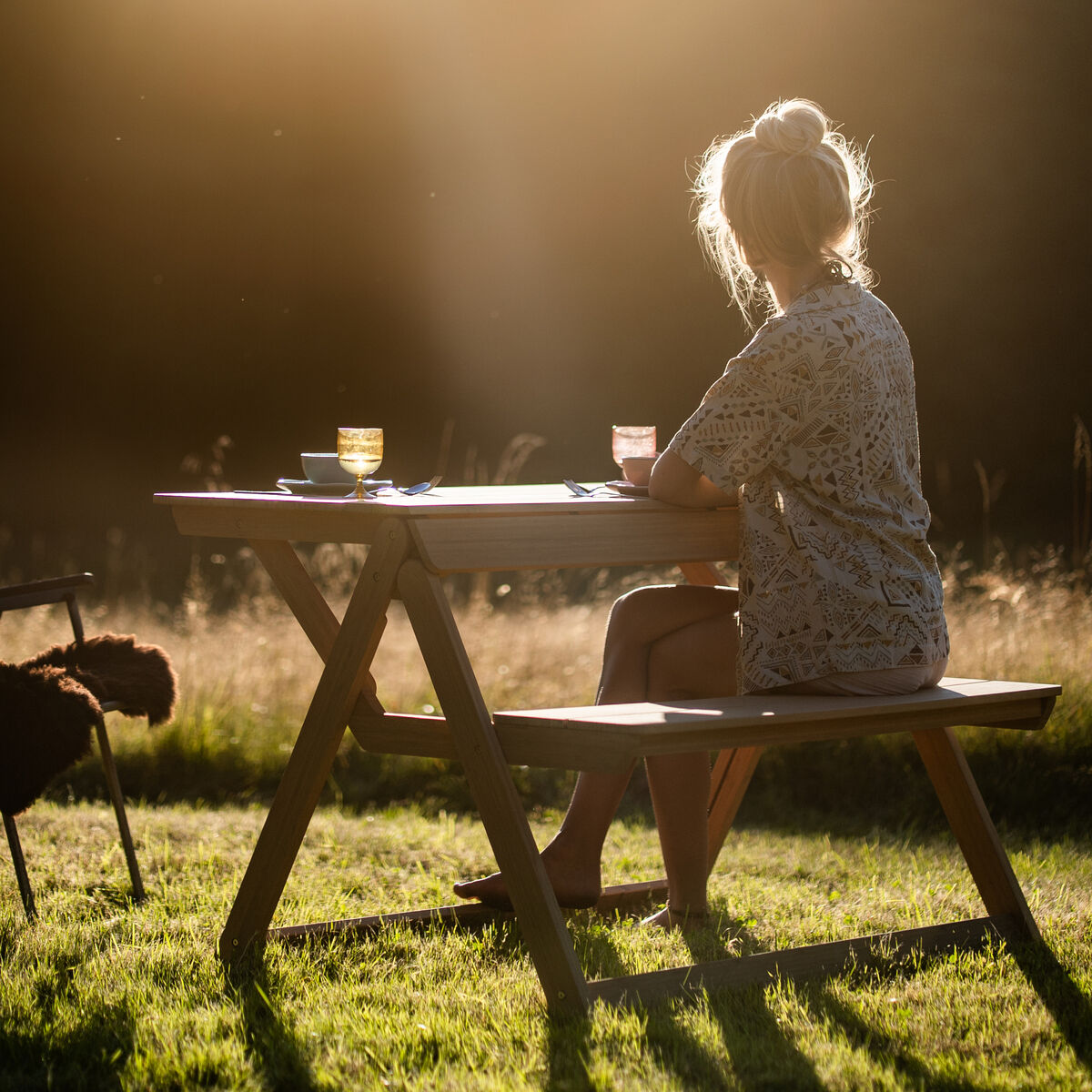 Braune, klappbare Tischbank „Folding Picnic Table“ der Marke Weltevree steht auf grünem Rasen vor neutralem Hintergrund. Die Bank ist aus Bambus gefertigt, kombiniert Sitzfläche und Tisch in einem klaren, funktionalen Design. Natürliche Holzmaserung ist sichtbar.