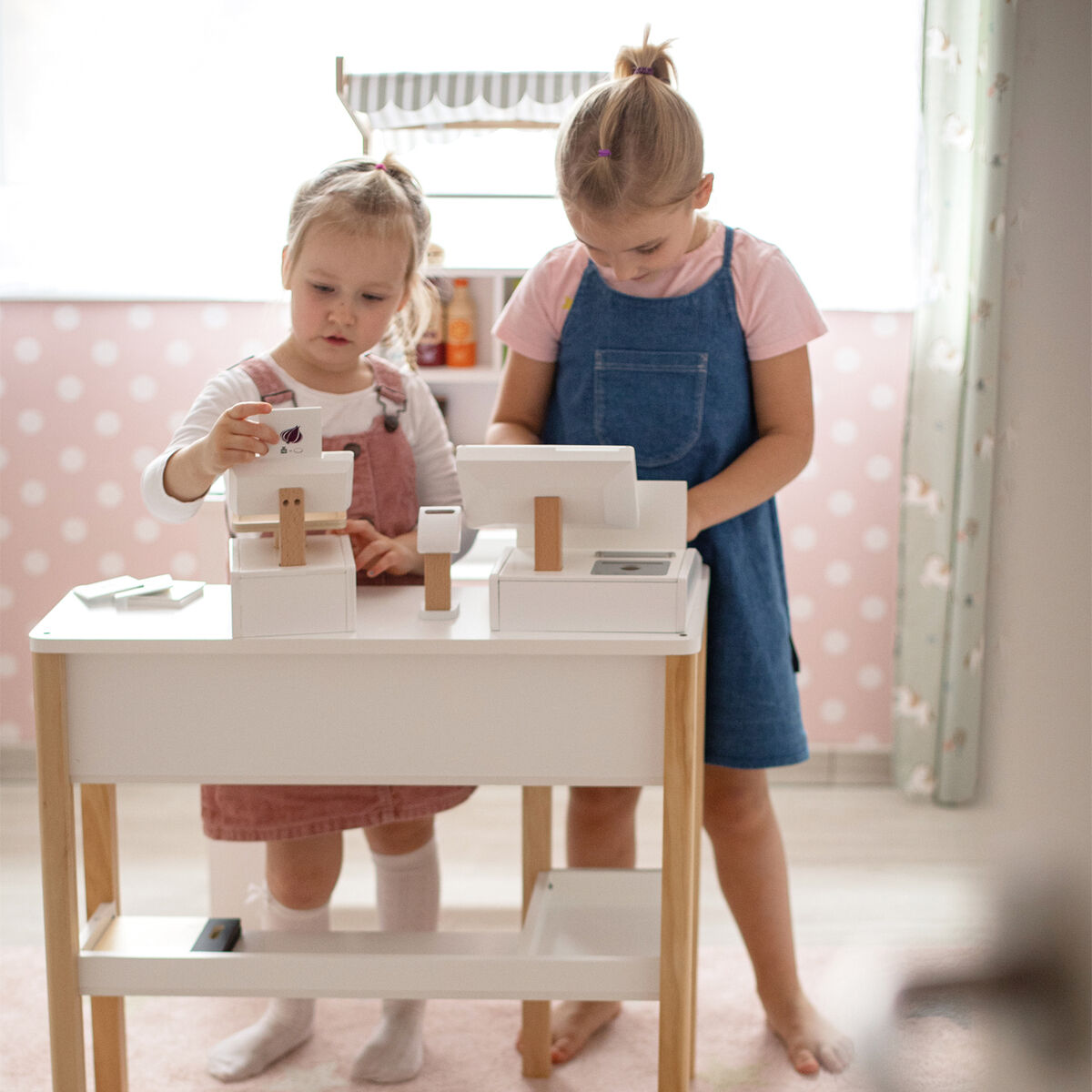 Zwei junge Mädchen spielen mit der Waage »Fresh« in einem liebevoll eingerichteten Kinderzimmer. Die Waage ist aus Holz und in dezenter, heller Farbpalette gestaltet, passend zu dem hellen Raum.