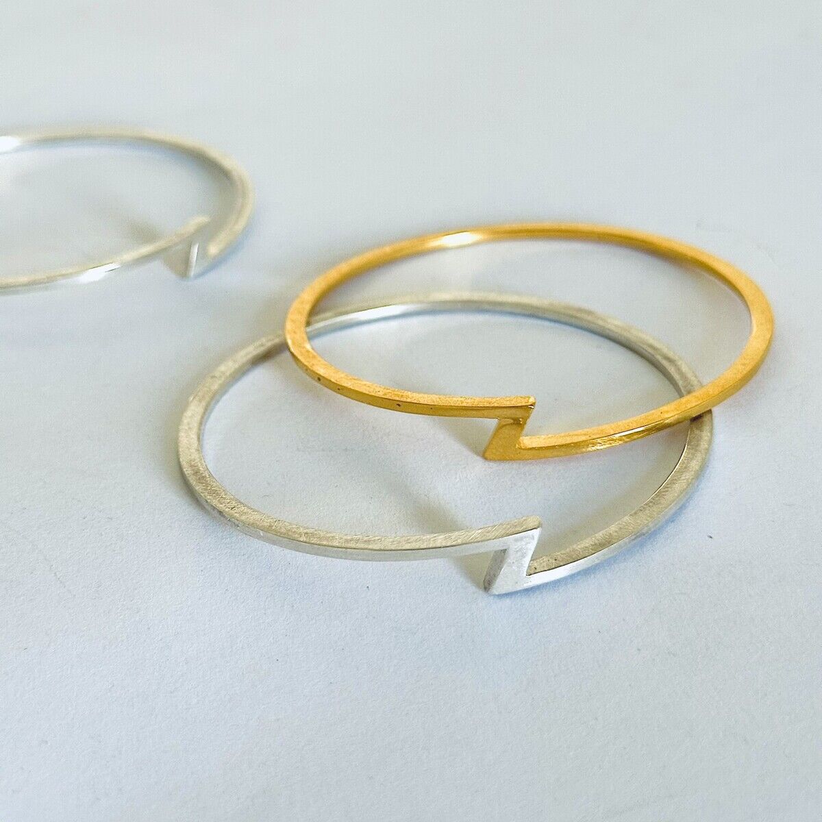 Zwei elegante Armreife auf hellem Untergrund: einer aus silbernem und einer aus feingoldplattiertem Silber. Beide sind offen gestaltet und stammen aus der ZEIT Sonderedition von HML Berlin. Die Armreife wirken modern, minimalistisch und hochwertig verarbeitet.
