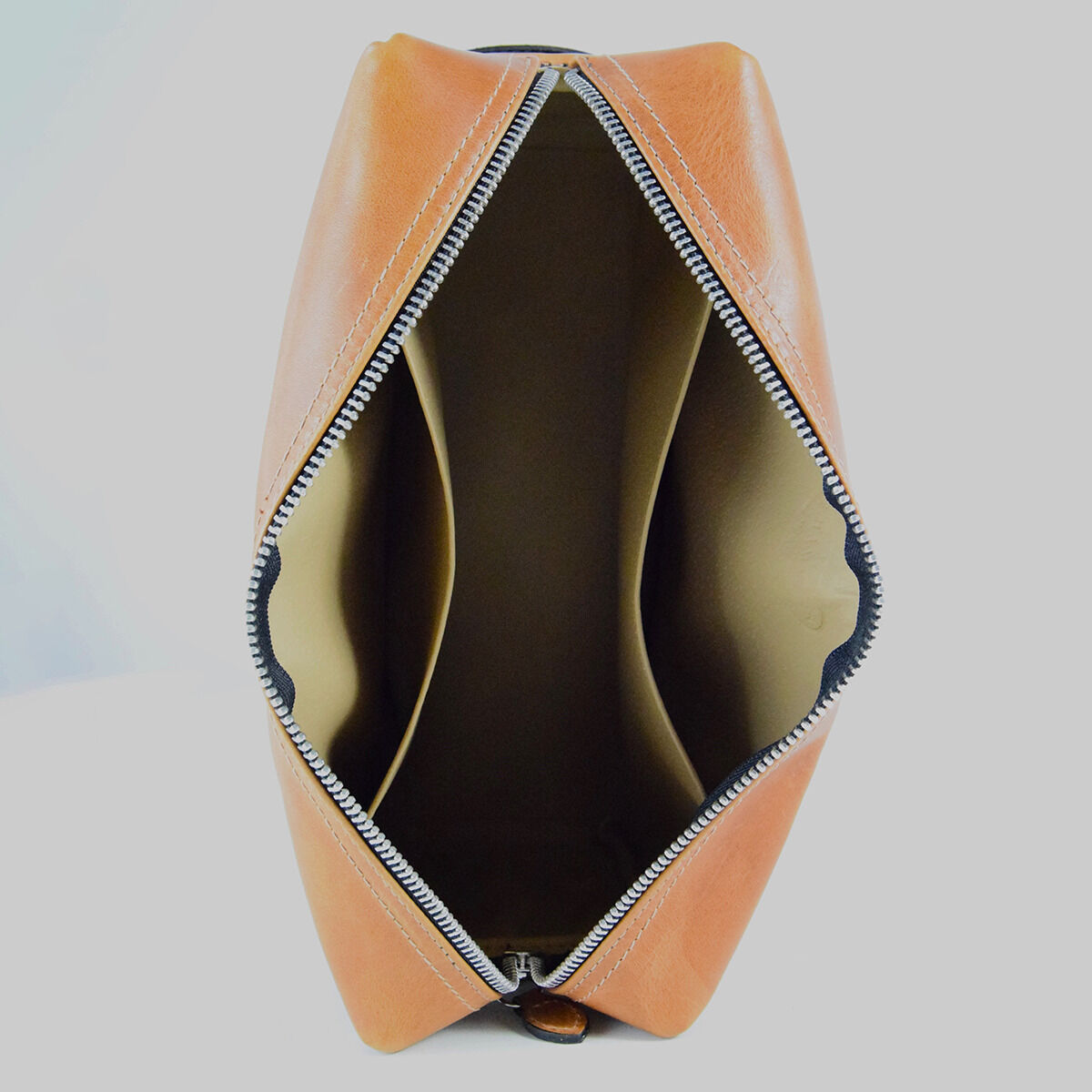 Braune Ledertasche mit Reißverschluss, geöffnet, gezeigt auf hellem Hintergrund. Die Innenseite ist in einem hellen Beigeton gehalten.