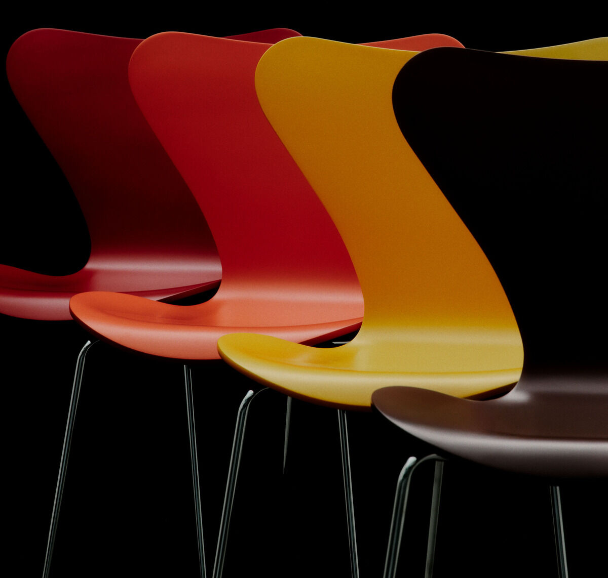 Vier Stühle der Serie 7 Edition Verner Panton von Fritz Hansen stehen schräg versetzt in einer Linie. Die Schalen bestehen aus farbig lackiertem Buchenfurnier in Gelb, Orange und Rot auf silbernem Stahlrohrgestell, vor schwarzem Hintergrund.