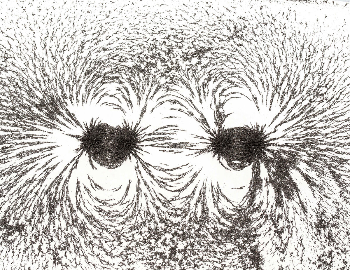 Eine Abbildung von magnetischen Feldlinien erzeugt durch zwei Magneten, die durch schwarze Eisenspäne auf einem weißen Hintergrund sichtbar gemacht werden.