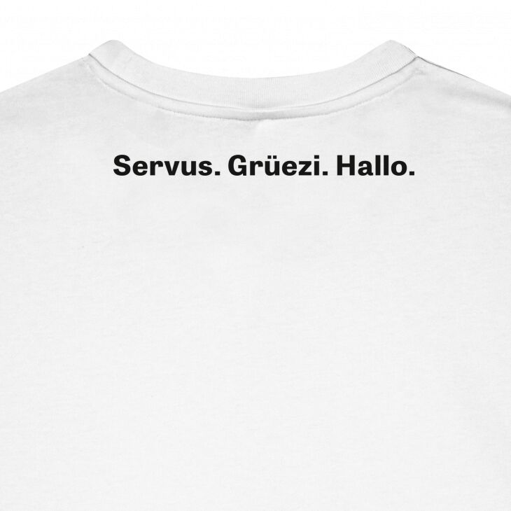 Weißes T-Shirt mit schwarzem Aufdruck 'Servus. Grüezi. Hallo.' am oberen Rücken, fotografiert von hinten auf neutralem Hintergrund, schlichtes und modernes Design.