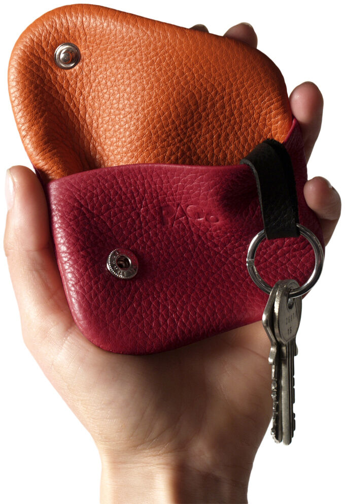 Hand hält zwei kleine Schlüsseletuis aus Leder in Orange und Rot, eines mit einem Schlüsselring und Schlüssel.