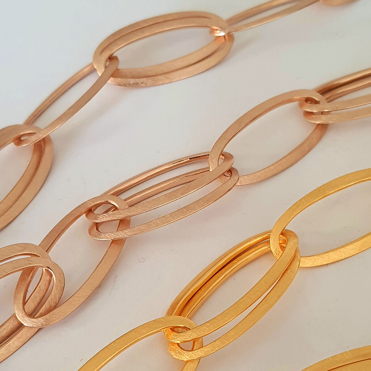 Mehrere ovale Colliers in verschiedenen Goldtönen nebeneinander auf hellem Untergrund. Die Ketten, darunter das Collier »GRACE« von HML Berlin in Roségold, zeigen glatte, mattierte Oberflächen und eine handgefertigte Verarbeitung. Modernes, elegantes Schmuckdesign.