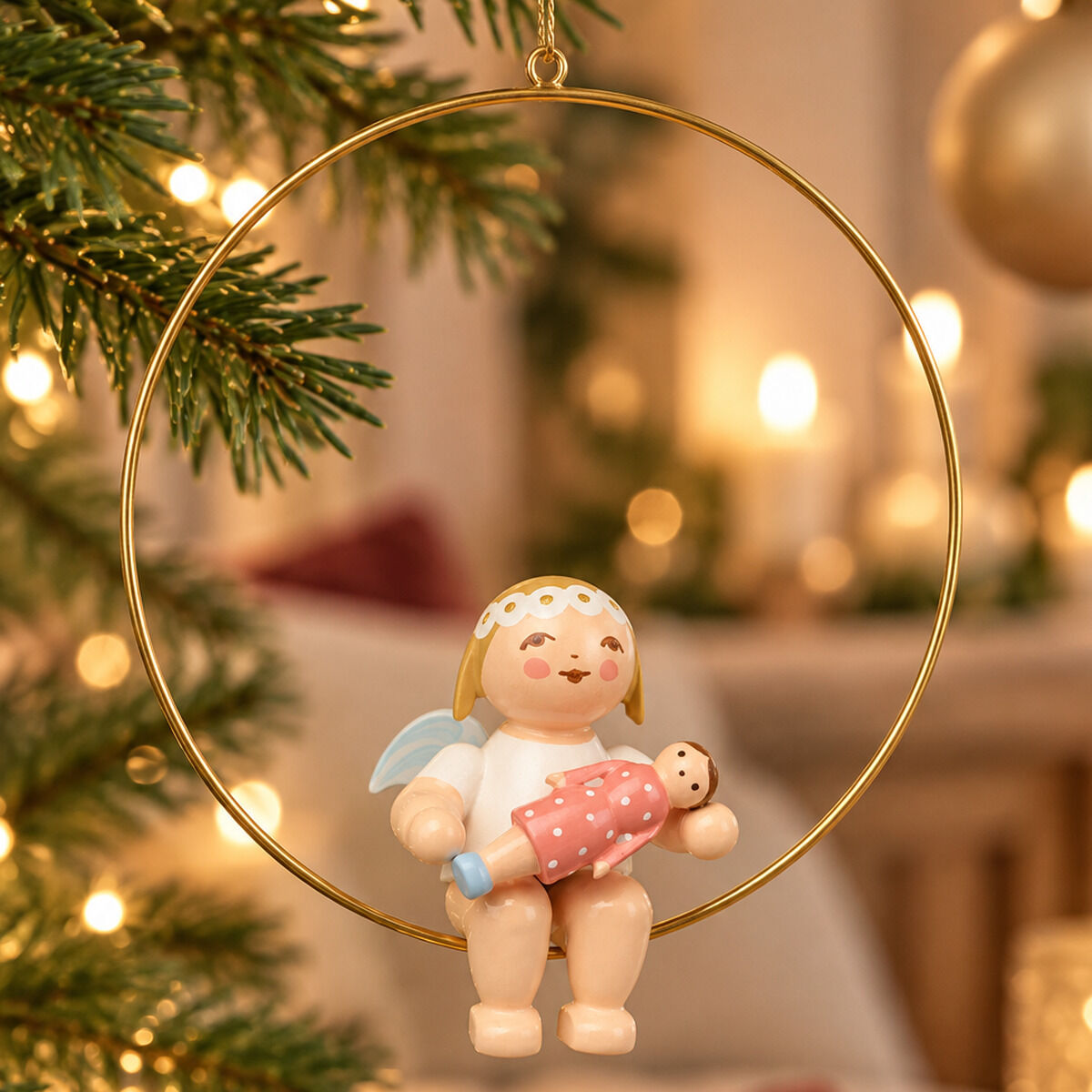Detailreiche Aufnahme einer handbemalten Holz-Figur »Christbaumengel im Ring, mit Puppe« von Wendt & Kühn, hängend im Weihnachtsbaum. Die Figur zeigt einen Engel mit blauer Flügeln und goldenen Haaren, der eine kleine Puppe hält. Im Hintergrund brennen Kerzen.