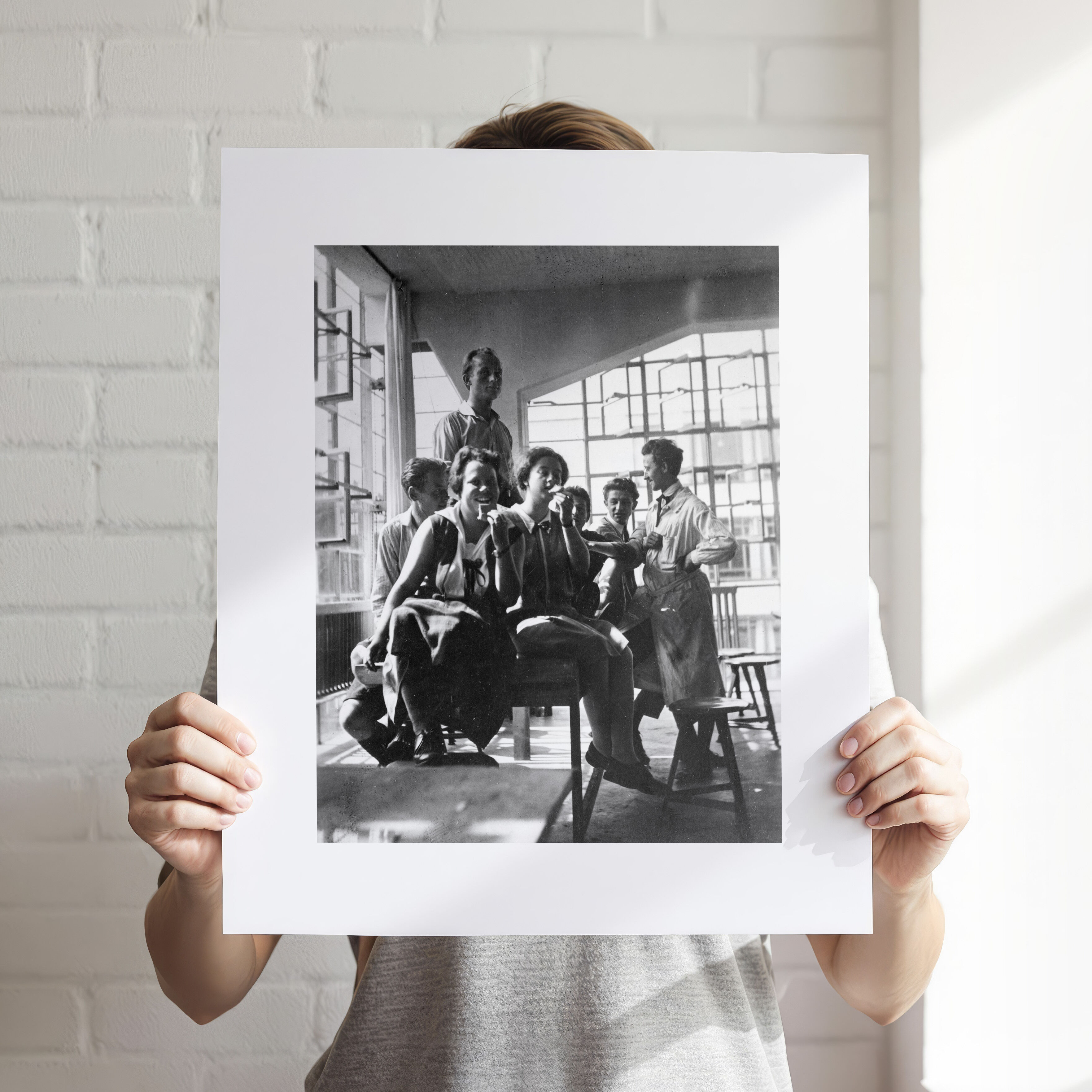 Kunstdruck mit schwarzweißer Fotografie aus dem Bauhaus Archiv Berlin, zeigt eine Gruppe von Menschen in modernistischer Architektur, gehalten von einer Person vor einer weißen Backsteinwand. Geeignet für Kunstliebhaber und an Bauhaus interessierte Personen. Das Bild betont Formen, Licht und Schatten in typischer Bauhaus-Ästhetik.