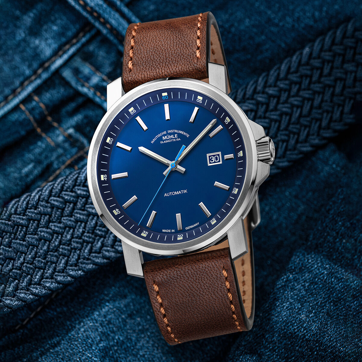 ZEIT-Sonderedition '29er Big Deep Blue' von Mühle-Glashütte: Luxuriöse Automatikuhr mit blauem Zifferblatt, braunem Lederarmband und Edelstahlgehäuse, stilvoll dargestellt auf einem blauen Hintergrund aus Jeansstoff.