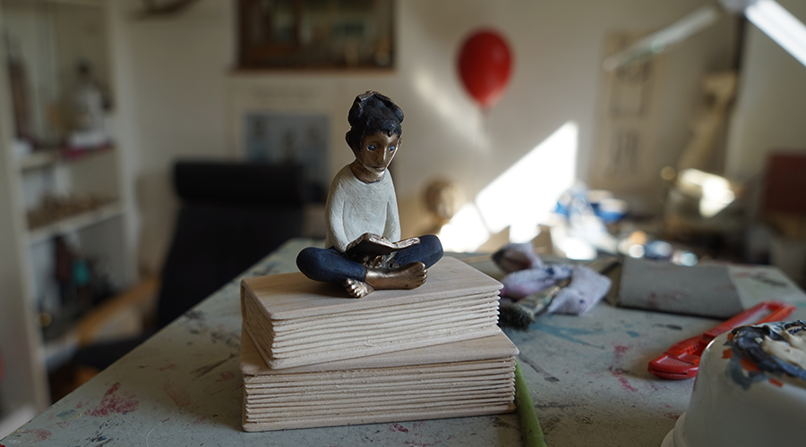 Kleine Skulptur einer sitzenden Person mit verschränkten Beinen auf zwei gestapelten Holzplatten in einem Atelier