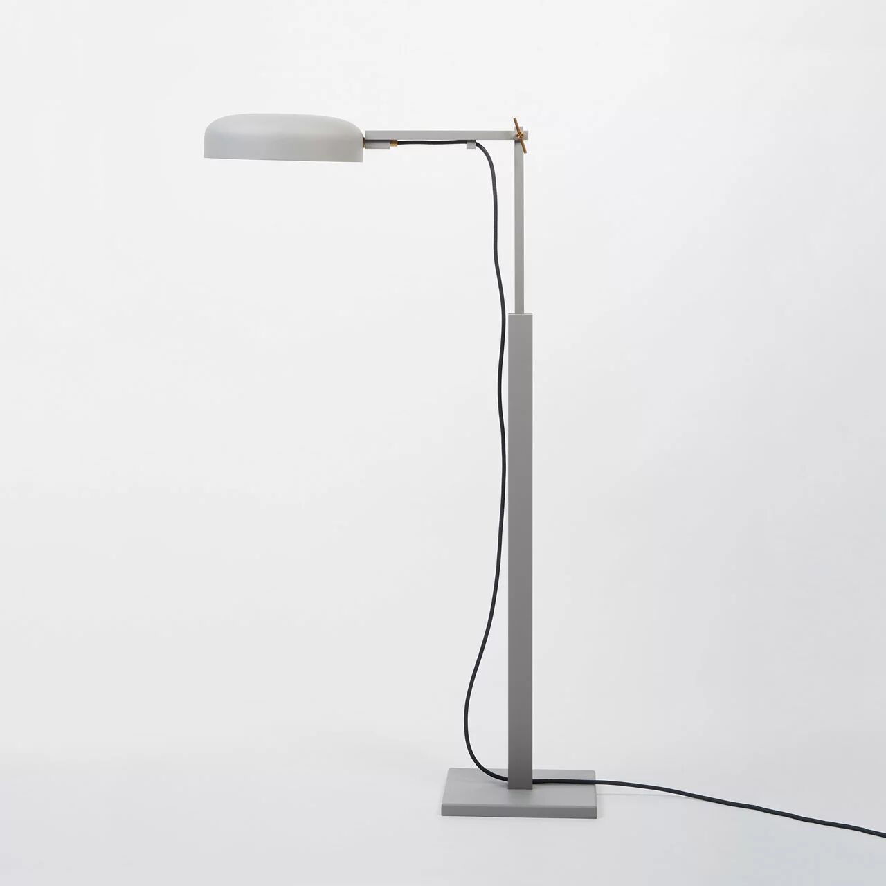 Die Stehleuchte »schliephacke« von mawa design steht freistehend auf einem rechteckigen, massiven Stahlguss-Fuß in Grau. Das Gestell ist aus Aluminium, die Leuchte hat einen runden, flachen Lampenschirm und ein schwarzes Kabel, das dekorativ am Gestell entlanggeführt ist.