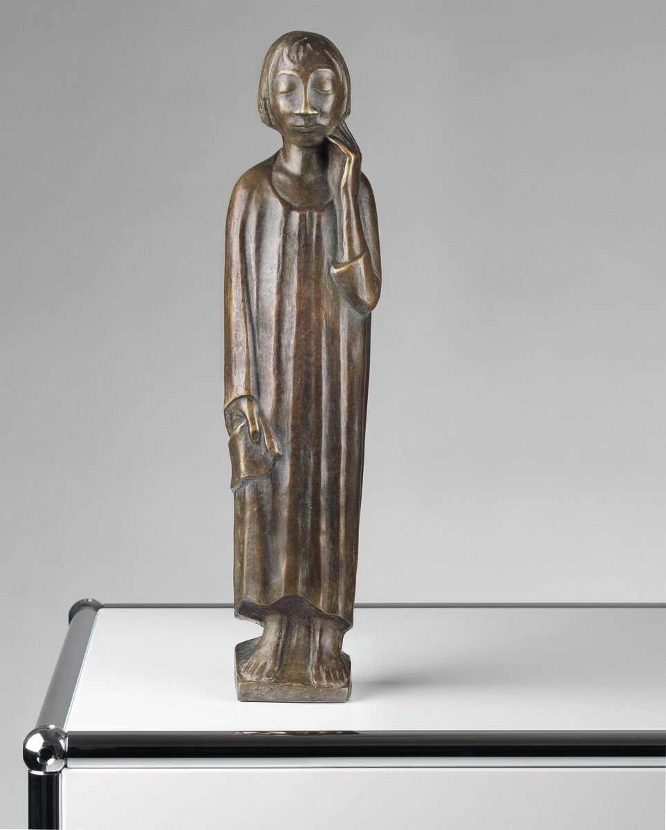 Eine Holzskulptur von Ernst Barlach aus dem Jahr 1934, genannt »Der Sinnende II«. Die Figur zeigt einen nachdenklichen Mann mit geschlossenen Augen und einer Hand an seiner Wange. Die Skulptur ist auf einer Metallplatte platziert und hat überwiegend braune und graue Farbtöne.