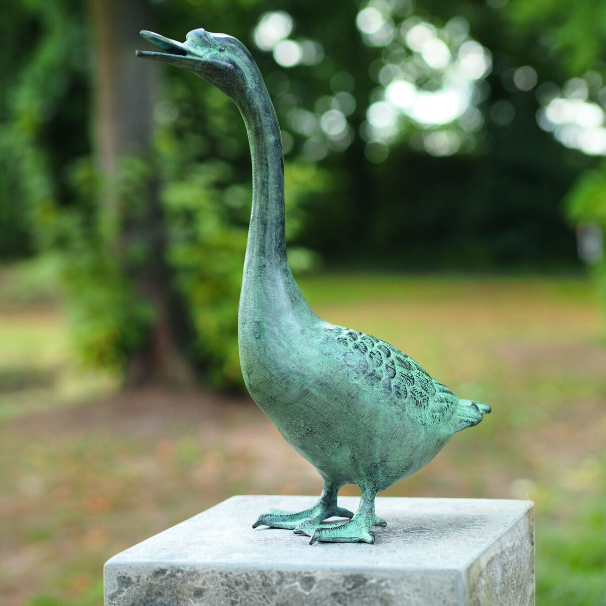 Eine Gartenskulptur in Form einer Gans namens Paula, in Bronzeoptik auf einem Sockel im Garten positioniert.