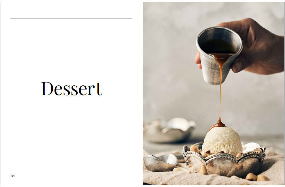 Kochbuch 'Sonntagsessen' mit einer Abbildung von Dessert. Eine Hand gießt Sirup über eine Kugel Eiscreme, die in einer Muschelschale angerichtet ist. Der Hintergrund ist neutral gehalten in beige und grauen Tönen.