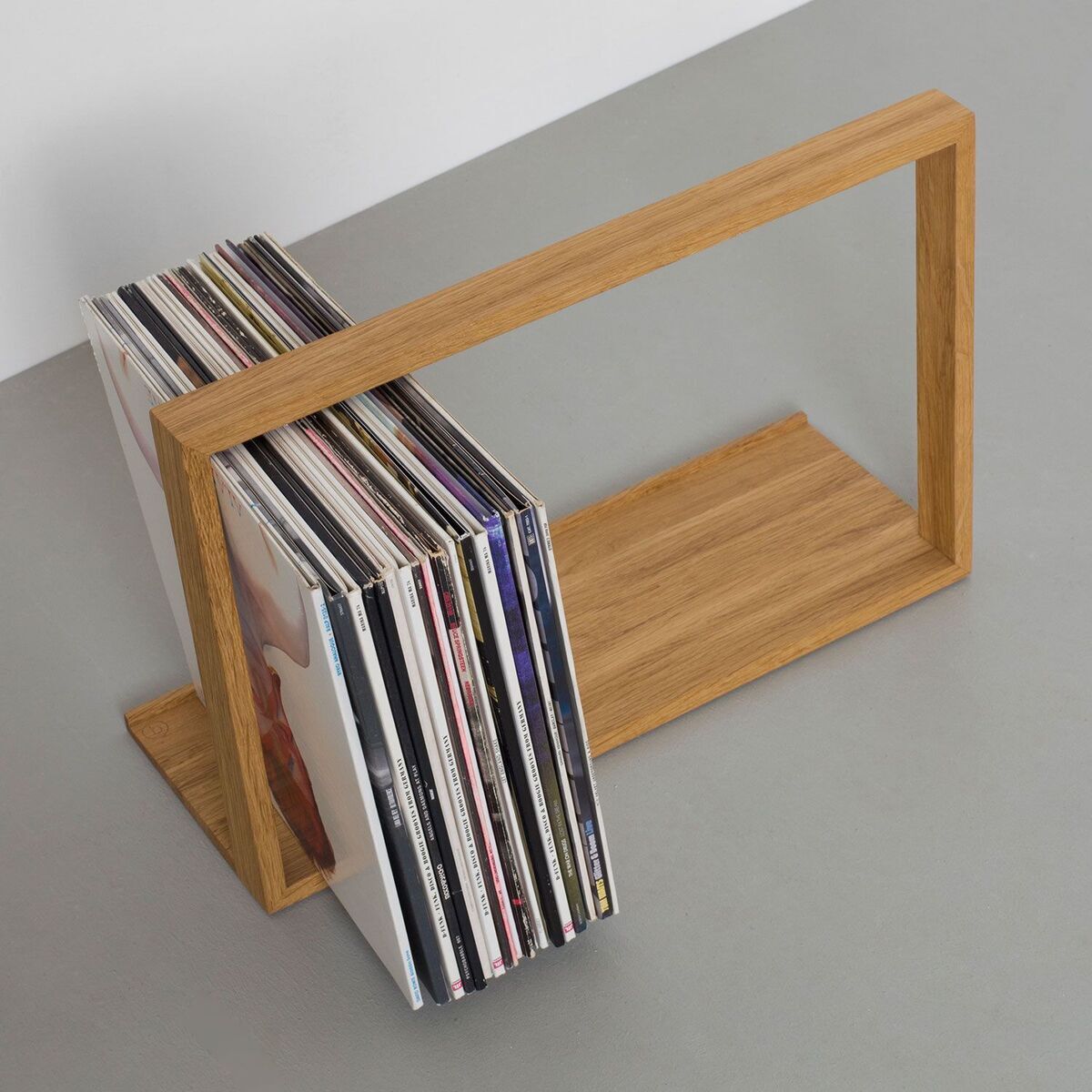 Ein moderner Schallplattenständer aus Holz, der eine Reihe von Schallplatten in einem minimalistischen Design aufbewahrt. Der Ständer hat eine rechteckige Form, die Vertikalflächen zur Unterstützung der Schallplatten bietet.