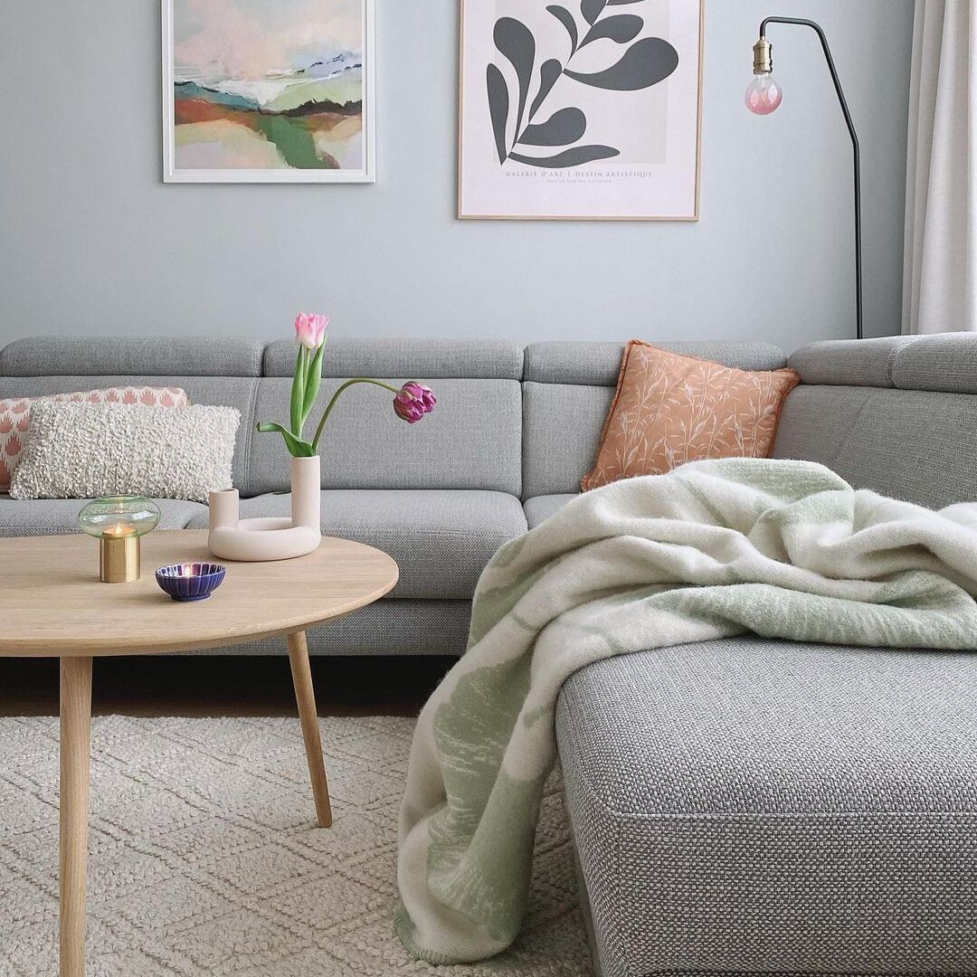 Ein Wohnzimmer mit einer grauen Couch, dekoriert mit einer Ginkgo-Decke und Kissen. An der Wand hängen zwei gerahmte Bilder. Der Raum wirkt modern und minimalistisch.