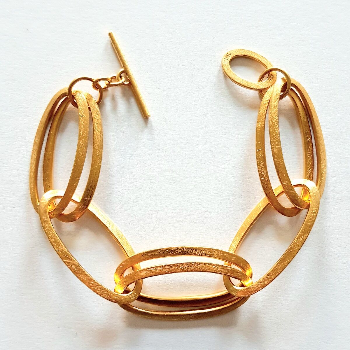Ein elegantes, goldenes Armband bestehend aus miteinander verbundenen ovalen Gliedern mit einem T-Verschluss, das auf einem weißen Hintergrund fotografiert wurde.