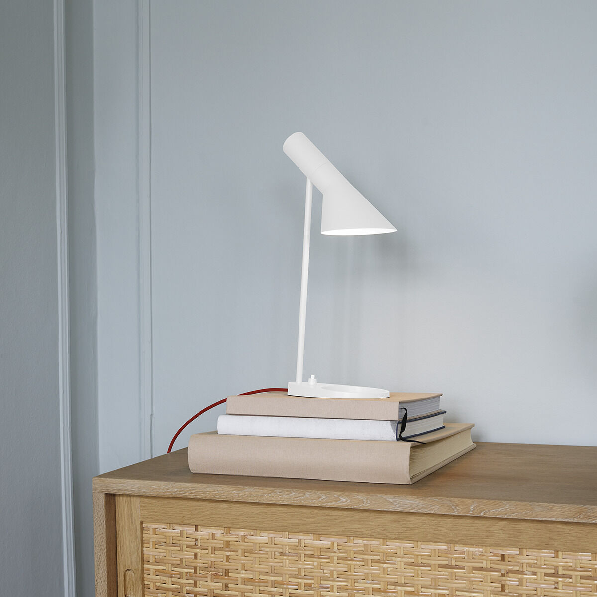Die ZEIT-Sonderedition Tischleuchte »AJ mini« in Weiß und Rot steht auf einer hellen Holzoberfläche. Die minimalistische Lampe hat einen schlichten, modernen Designstil.