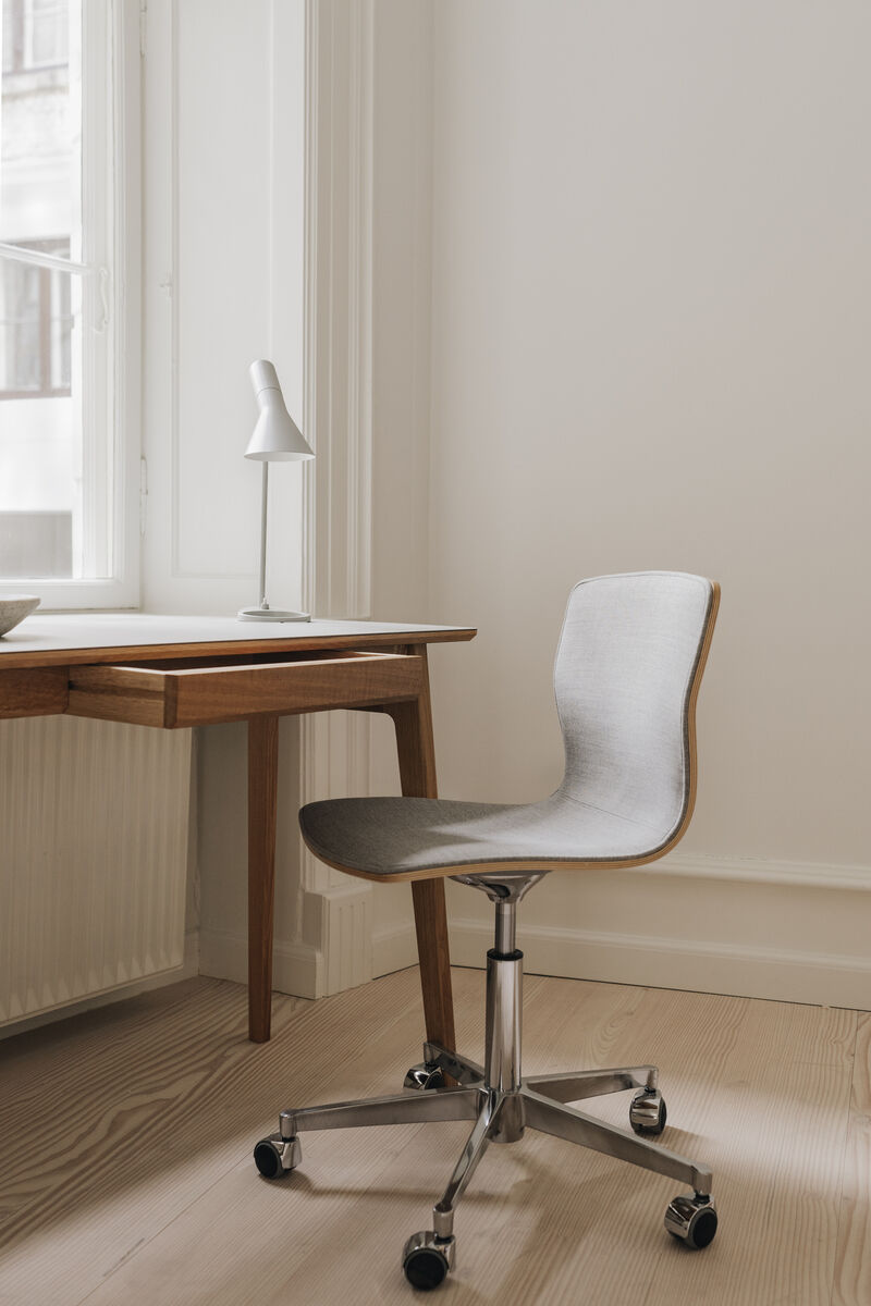 Ein moderner Schreibtisch aus Eiche mit minimalistischen Design, dazu passend ein hellgrauer Bürostuhl auf Rollen vor einem großen Fenster.