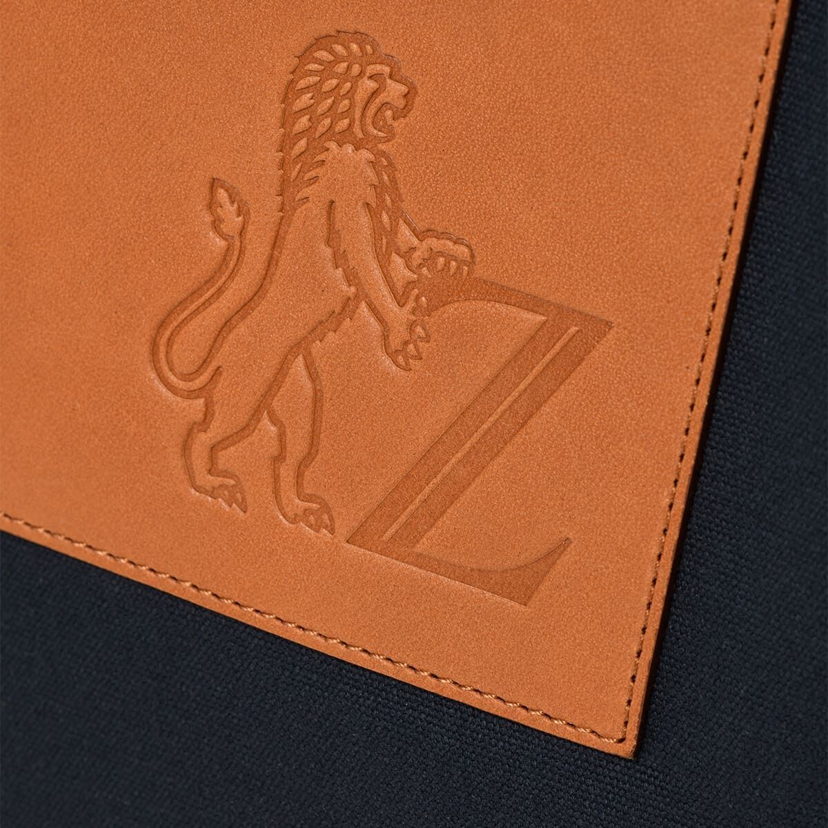 Nahaufnahme einer hochwertigen braunen Ledertasche mit dem geprägten Logo eines stehenden Löwen, der einen Buchstaben 'Z' hält. Die Tasche hat einen eleganten und edlen Look und ist im ZEIT Shop erhältlich.