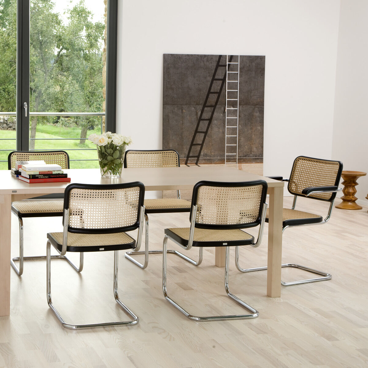 Modernes Esszimmer mit hellbraunem Holztisch und sechs Thonet S 32 Stahlrohr-Freischwinger Stühlen in Schwarz und Beige. Große Fenster mit Blick auf grüne Landschaft im Hintergrund. Stilvolles und minimalistisches Design.