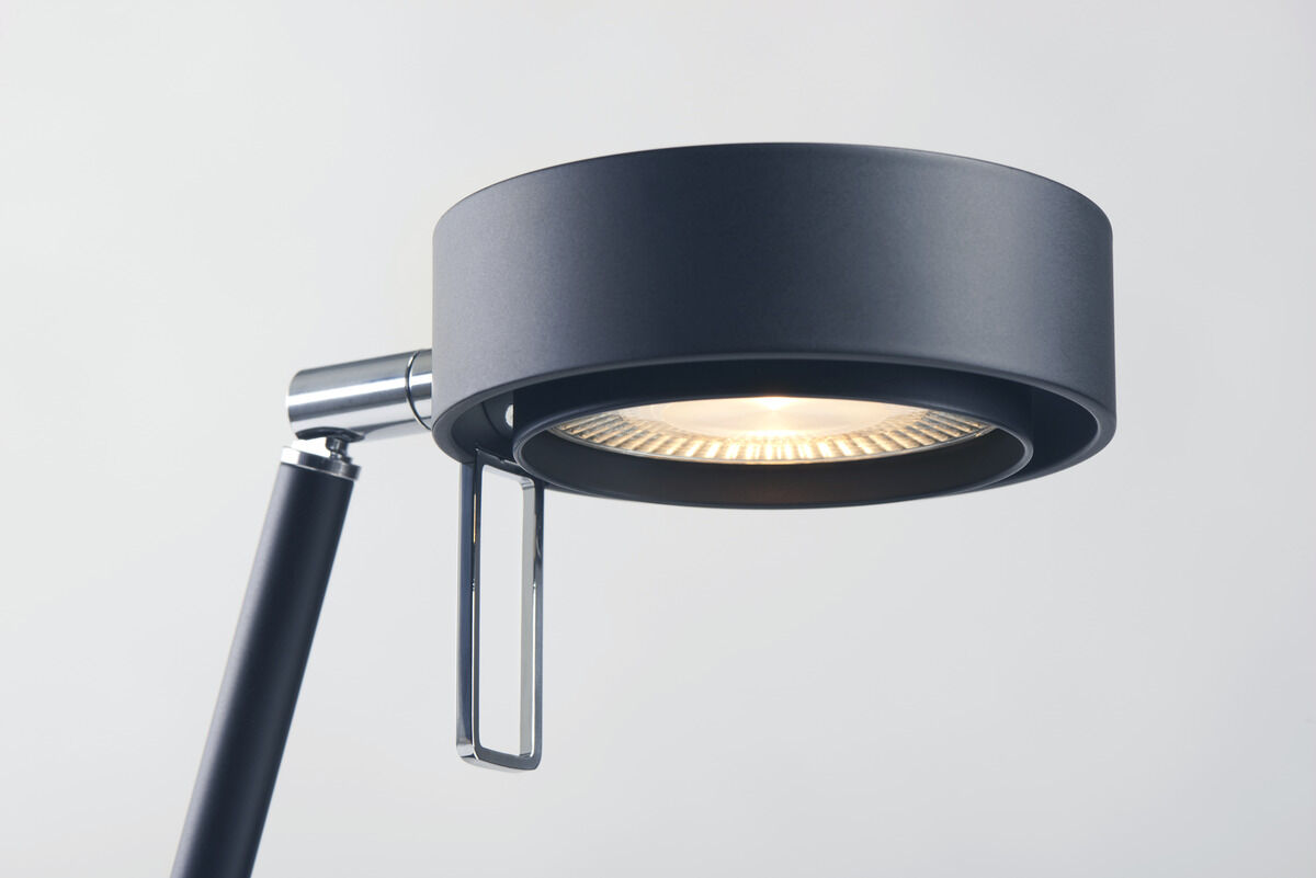 Schwarze, moderne Tischleuchte mit Chromteilen und minimalistischem Design. Die Leuchte hat einen runden Leuchtkopf und eine metallische Halterung.