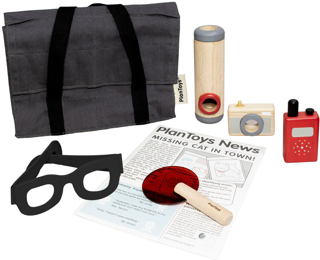 Ein Detektiv-Set bestehend aus einer Grauen Tasche mit schwarzen Trägern, einer Lupe, einem Fernglas, einem Walkie-Talkie, einer Kamera, einer Nachrichten-Zeitung und einer Lupe mit rotem Griff, alles aus Holz.