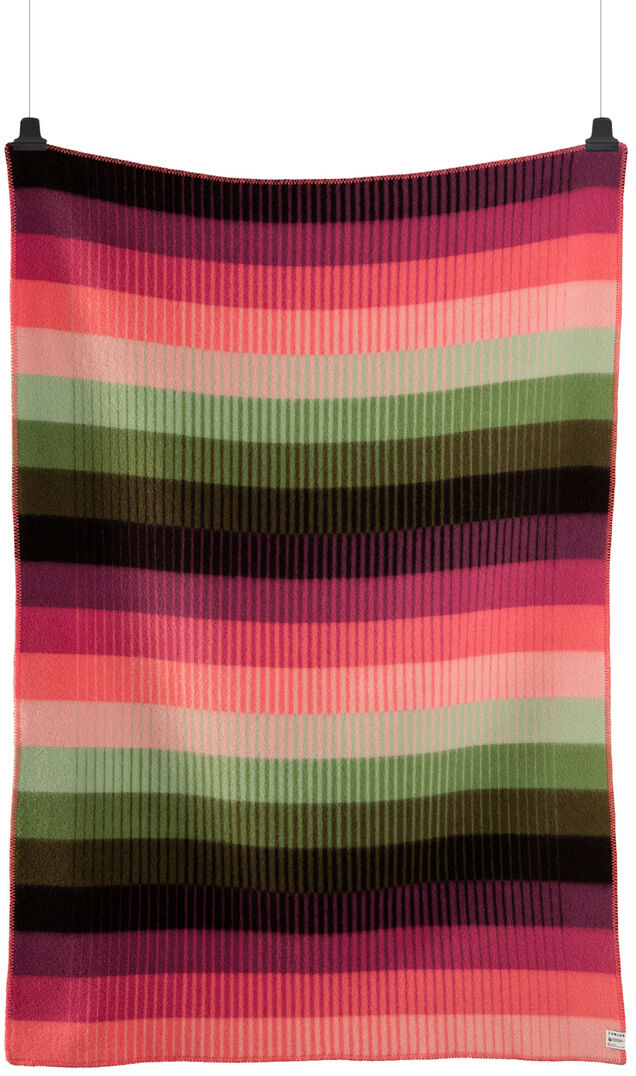 Eine bunte Wolldecke aus Lammwolle mit dem Namen »ASMUND Grad«. Die Decke ist gestreift in den Farben Pink, Grün, Schwarz, Rosa, Weiß und Braun und hängt gerade an zwei Haken.