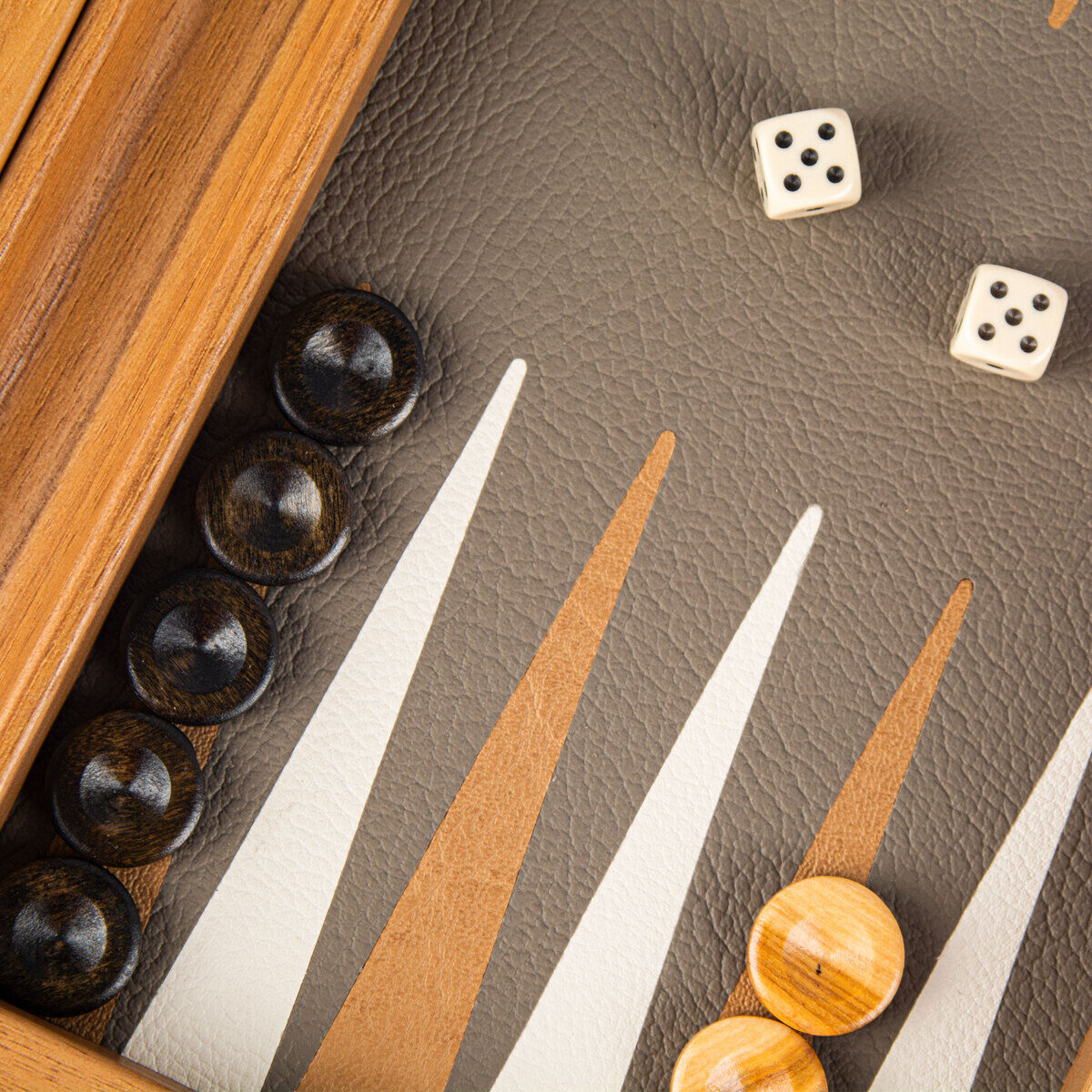 Nahaufnahme eines Reise-Backgammon-Spiels mit einem Holzrahmen, grauem und beigem Spielbrett in Straußenleder-Optik, schwarzen und hellen Spielsteinen sowie zwei Würfeln.