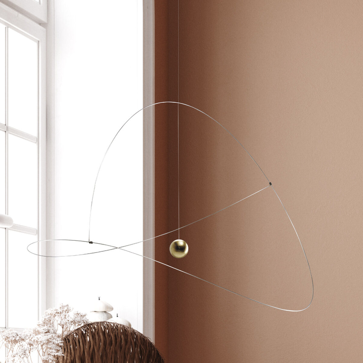Das Mobile »Metamorphosis, Golden Planet« von Flensted Mobiles schwebt filigran vor einem hellen Fenster, mit feinen Edelstahldrähten und einer goldenen Kugel als Mittelpunkt, moderne Wohnaccessoires und Deko auf der Fensterbank, warme Erdtöne im Raum.