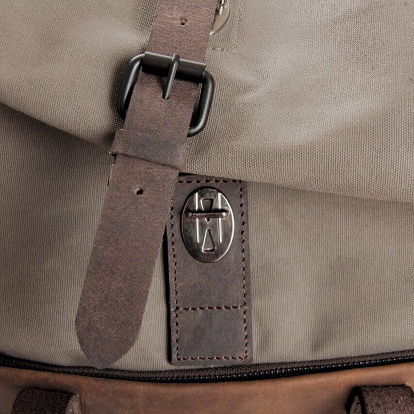Nahaufnahme eines Rucksacks »Twister« mit einem Ledergurt und einem Verschluss mit Metallschnalle. Der Rucksack kombiniert Stoff- und Lederdetails und ist in erdigen Farbtönen wie Braun, Beige und Dunkelgrau gestaltet.