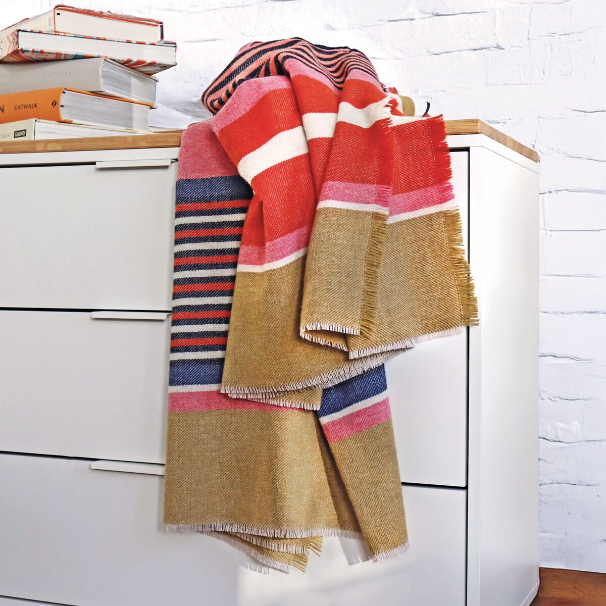 Die Merino-Decke »Rio« von Eagle Products liegt ausgebreitet und zeigt ihr farbenfrohes Streifenmuster in Sand, Gelb, Blau, Grün, Orange und Pink. Die Decke besitzt kurze Fransen an den Rändern und wirkt durch die kräftigen Farben lebendig, sommerlich und modern.