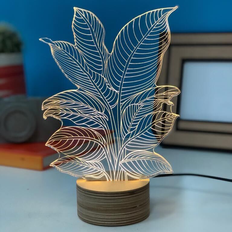 Eine dekorative 3D-Lampe in Form einer Heliconia-Pflanze. Die Lampe hat klar definierte Blätter, die in gelben LED-Lichtern leuchten. Die Basis ist rund und aus Holz gefertigt. Im Hintergrund sind unscharf Bücher und ein Bilderrahmen zu sehen, vor einer blau gestrichenen Wand platziert.