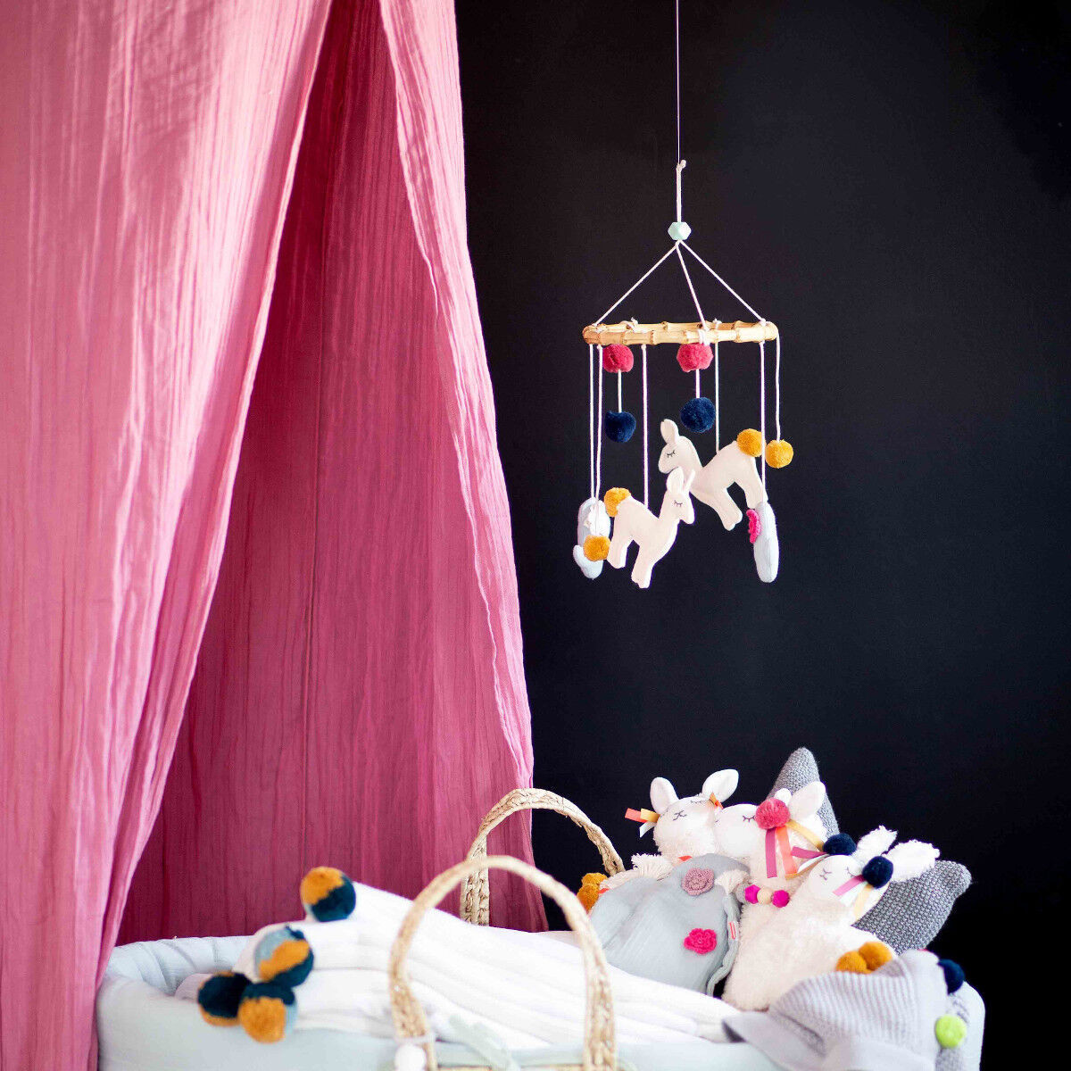 Ein rosa Betthimmel für Kinder, aufgehängt über einem gemütlichen Spielbereich. Ein hängendes Mobile mit bunten Pompons und Tierfiguren ist im Vordergrund. Der Hintergrund ist in dunklen Farben gehalten.