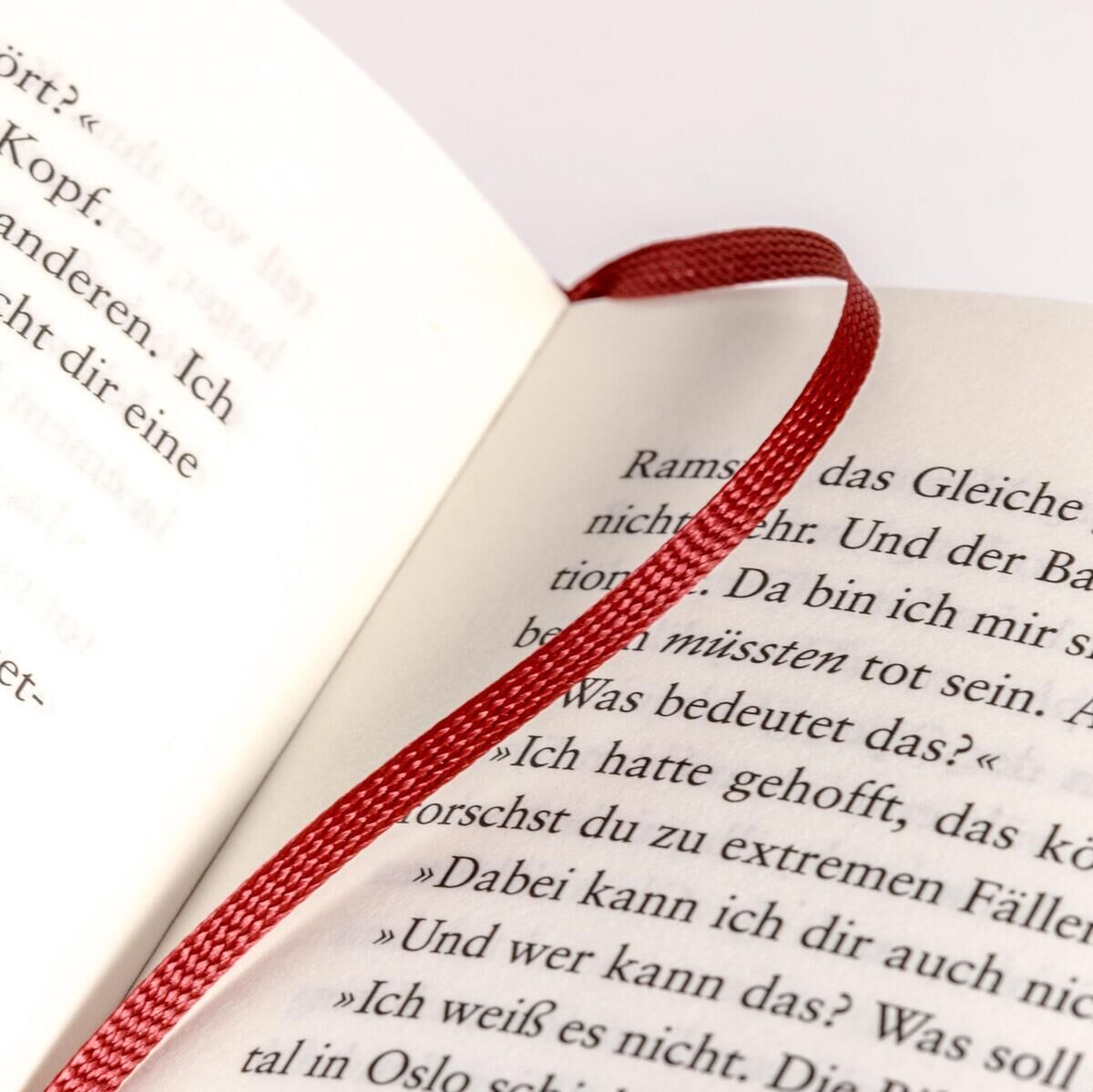 Ein aufgeschlagenes Buch mit einem roten Lesezeichen liegt offen. Auf den Seiten ist gedruckter Text sichtbar.