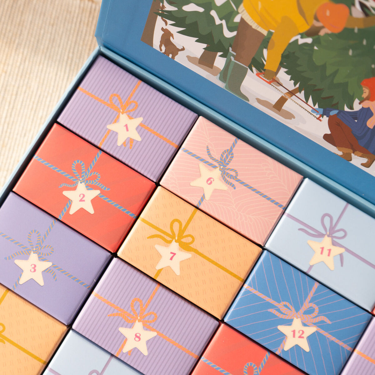 Adventskalender mit 12 bunten, einzeln verpackten Geschenkboxen in verschiedenen Farben, alle mit einer Nummer und Band dekoriert. Im Hintergrund ist eine Illustration von Menschen zu sehen, die Weihnachtsbäume auswählen. Thema: Weihnachten und Winterzeit.