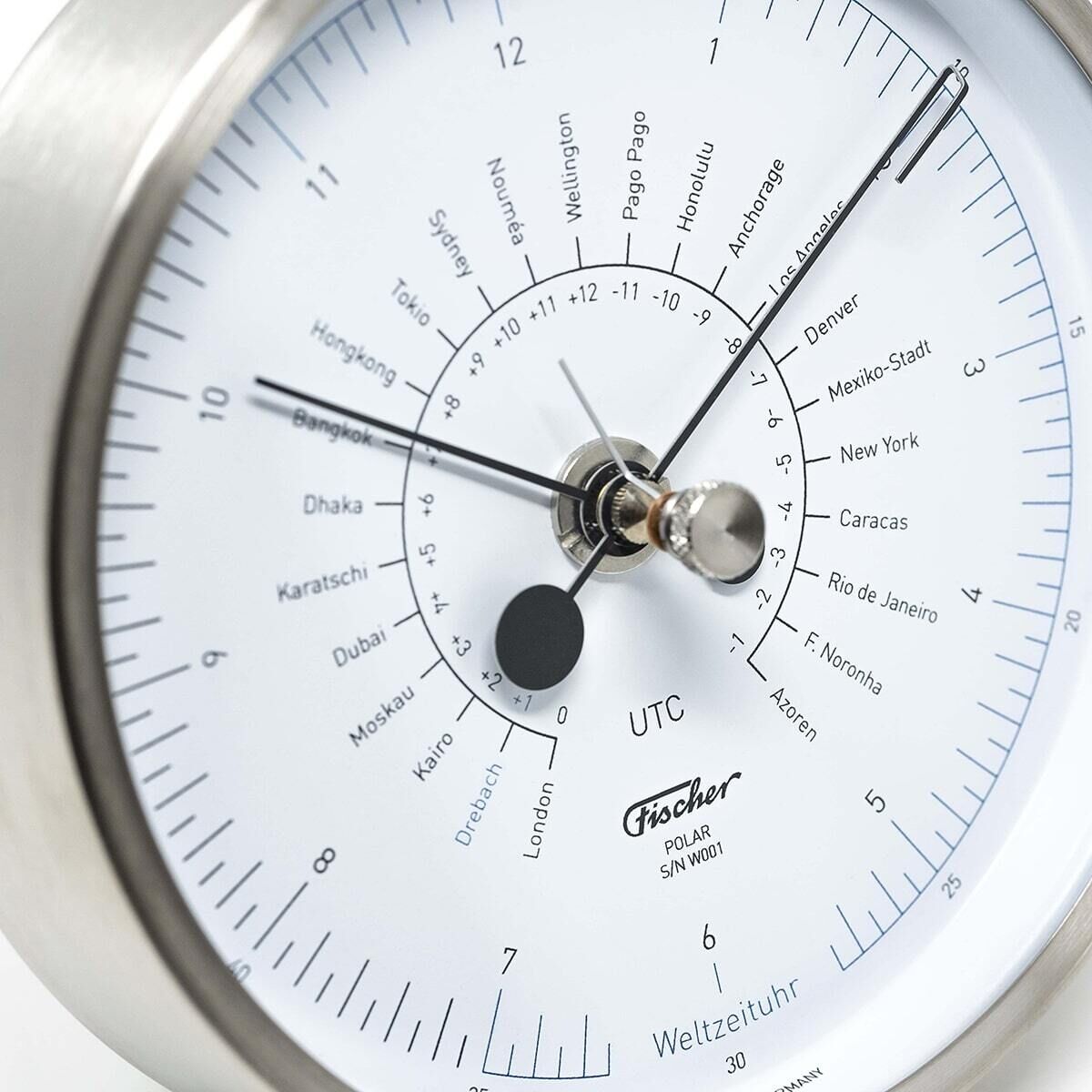 Nahaufnahme einer Weltzeituhr des Modells POLAR von Fischer Manufaktur. Die Uhr zeigt verschiedene Zeitzonen an und hat ein schlichtes Design mit überwiegend silbernen, weißen und schwarzen Farben. Sie besitzt ein kreisförmiges Zifferblatt und ist aus hochwertigen Materialien gefertigt.