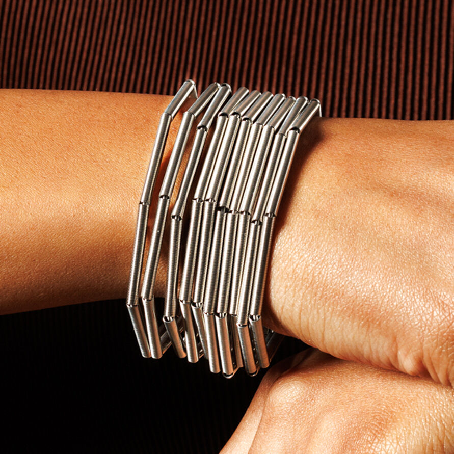 Detailaufnahme eines silberfarbenen Edelstahlarmbands 'MISTY' von la molla am Handgelenk einer Person, vor braunem, geripptem Hintergrund. Das Armband besteht aus mehreren filigranen Stäben mit modernem, geometrischem Design und wirkt edel und stilvoll.